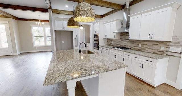 kitchen featuring white cabinetry, wall chimney exhaust hood, a kitchen island with sink, and decorative light fixtures