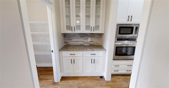 kitchen with tasteful backsplash, light stone counters, light hardwood / wood-style floors, white cabinets, and appliances with stainless steel finishes