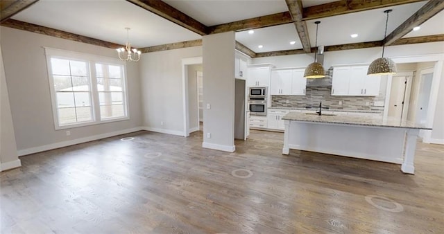 kitchen featuring light stone counters, sink, decorative light fixtures, white cabinetry, and an island with sink