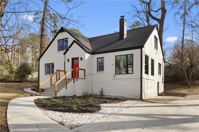 view of front facade with a chimney, a shingled roof, and stone siding