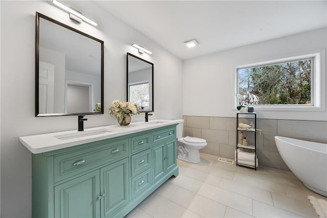 full bath featuring tile walls, a soaking tub, double vanity, toilet, and tile patterned floors