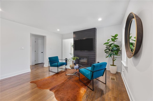living area with a large fireplace, wood finished floors, baseboards, and recessed lighting