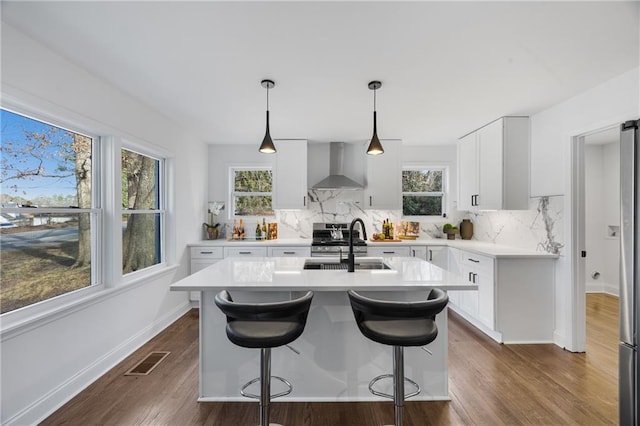 kitchen with wall chimney exhaust hood, a sink, backsplash, light countertops, and dark wood-style floors