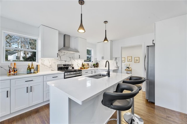 kitchen featuring appliances with stainless steel finishes, wall chimney range hood, a sink, decorative backsplash, and a kitchen bar