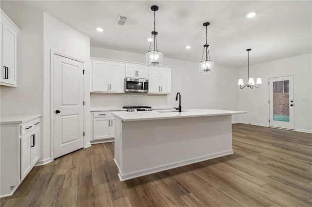 kitchen featuring stainless steel microwave, light countertops, a sink, and wood finished floors