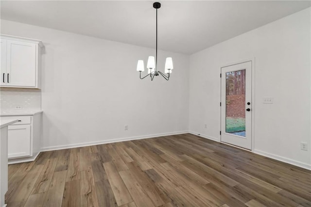 unfurnished dining area featuring an inviting chandelier, wood finished floors, and baseboards