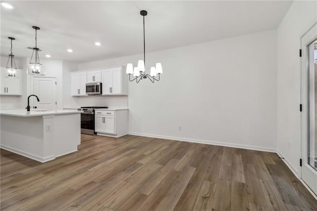 kitchen with light countertops, appliances with stainless steel finishes, white cabinetry, a sink, and wood finished floors