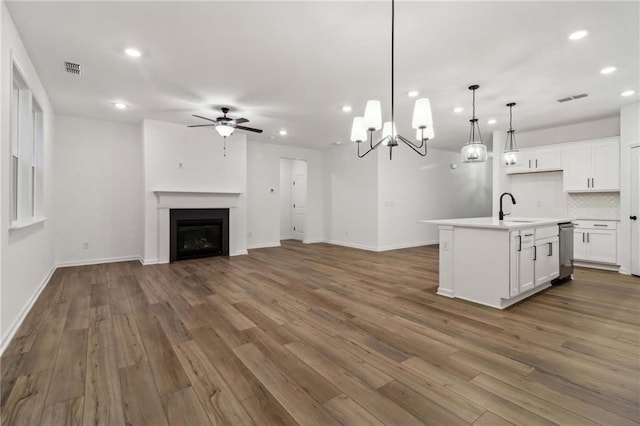 kitchen featuring a fireplace, open floor plan, white cabinetry, a sink, and wood finished floors