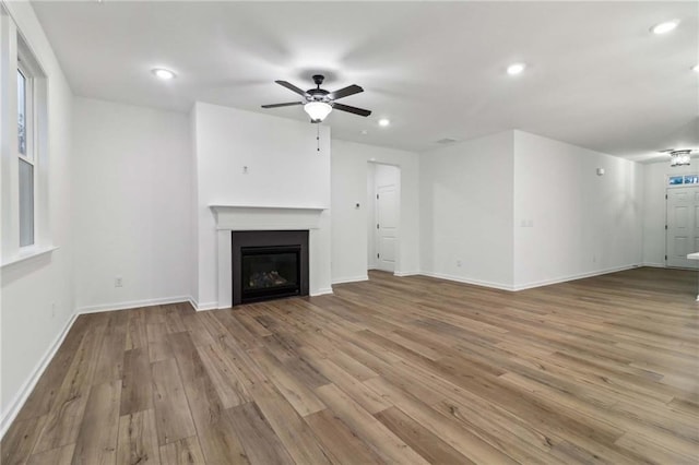 unfurnished living room with baseboards, a glass covered fireplace, ceiling fan, wood finished floors, and recessed lighting