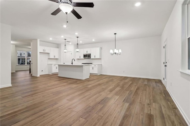 unfurnished living room with recessed lighting, baseboards, light wood-style floors, a sink, and ceiling fan with notable chandelier