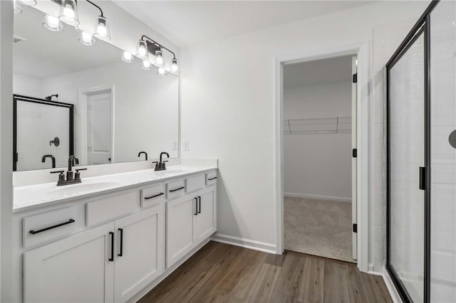 full bath with double vanity, a stall shower, wood finished floors, a spacious closet, and a sink