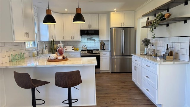 kitchen featuring a breakfast bar area, appliances with stainless steel finishes, a peninsula, white cabinetry, and a sink