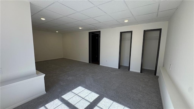 unfurnished bedroom featuring multiple closets, recessed lighting, baseboards, carpet flooring, and a paneled ceiling