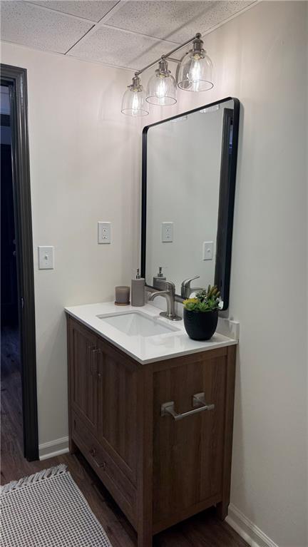 bathroom with a drop ceiling, vanity, baseboards, and wood finished floors