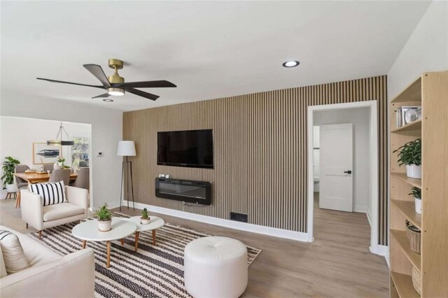 living area featuring an accent wall, a ceiling fan, baseboards, light wood-type flooring, and wallpapered walls