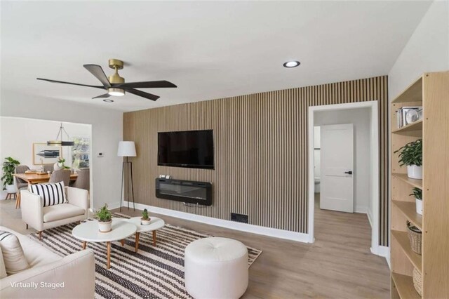 living area with wallpapered walls, baseboards, a ceiling fan, an accent wall, and light wood-style floors