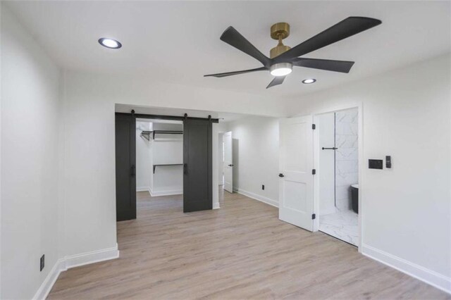 empty room featuring light wood-type flooring, ceiling fan, baseboards, and a barn door