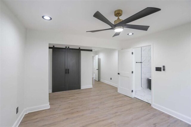 spare room with ceiling fan, a barn door, light wood-style flooring, and baseboards