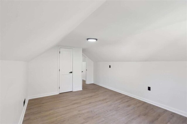 bonus room featuring lofted ceiling, light wood-style flooring, and baseboards