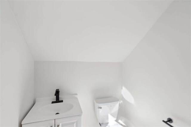 half bathroom with toilet, lofted ceiling, and vanity