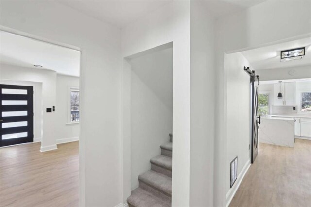 staircase featuring a barn door, wood finished floors, visible vents, and baseboards