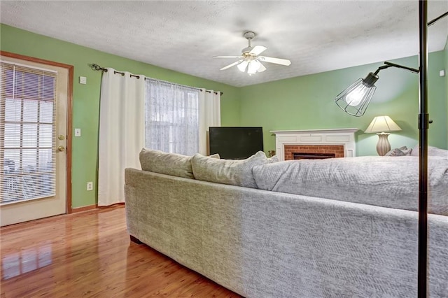 living room with hardwood / wood-style flooring, a fireplace, a textured ceiling, and ceiling fan