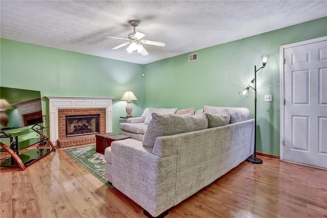 living room featuring a brick fireplace, a textured ceiling, ceiling fan, and light hardwood / wood-style flooring