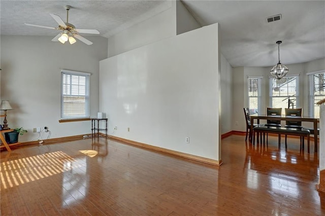 living room with hardwood / wood-style flooring, lofted ceiling, ceiling fan with notable chandelier, and a textured ceiling