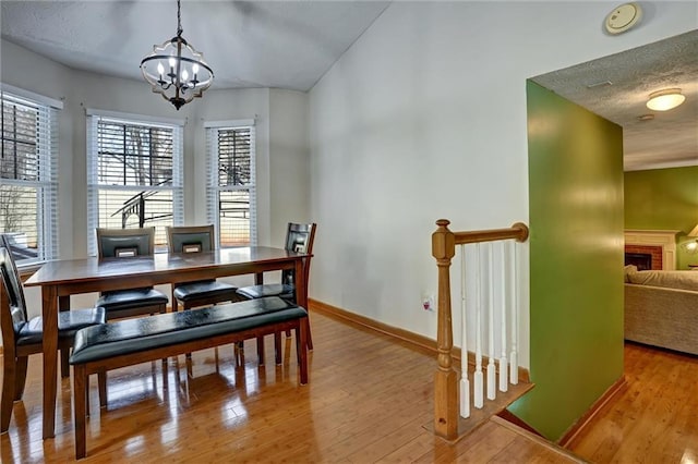 dining area featuring wood-type flooring, a textured ceiling, a brick fireplace, and a notable chandelier