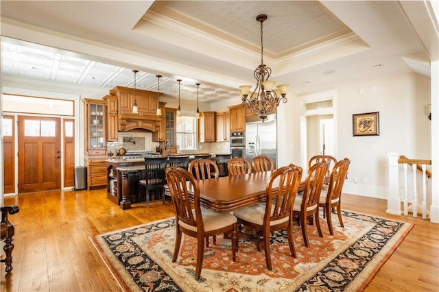 dining room featuring an inviting chandelier, ornamental molding, a raised ceiling, and light wood-type flooring