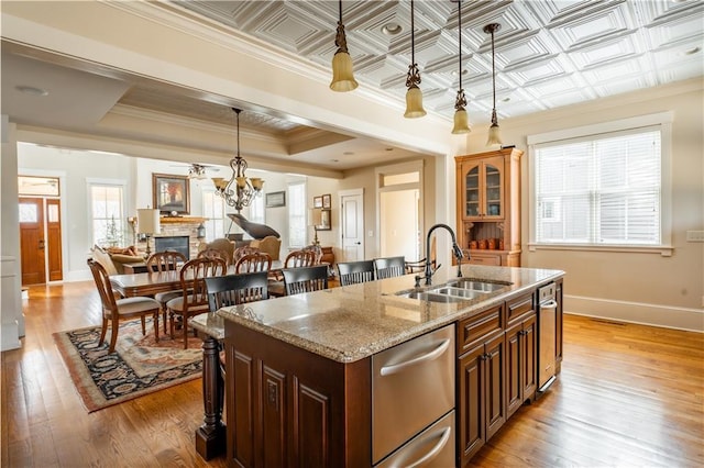 kitchen featuring a stone fireplace, decorative light fixtures, sink, light stone counters, and a center island with sink