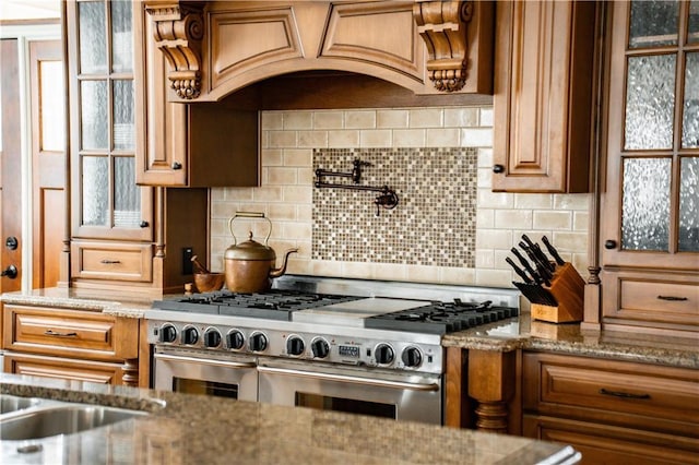 kitchen featuring light stone counters, range hood, range with two ovens, and backsplash