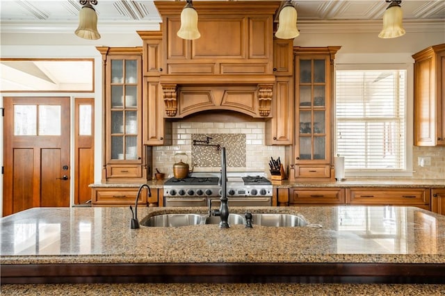 kitchen with a center island with sink, backsplash, light stone counters, and decorative light fixtures