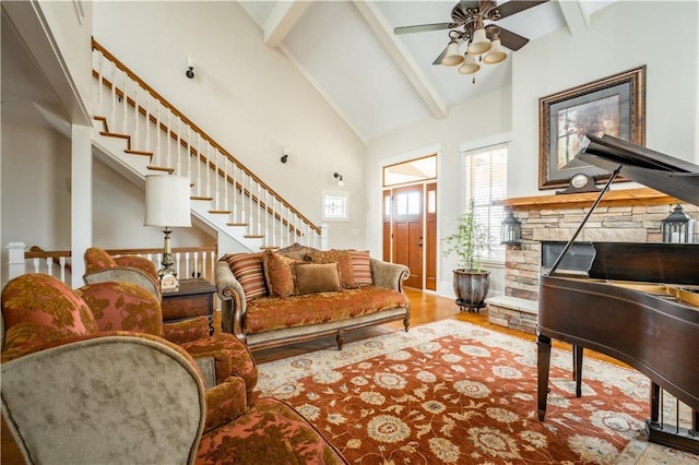 sitting room with a stone fireplace, high vaulted ceiling, ceiling fan, beam ceiling, and hardwood / wood-style floors