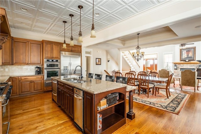 kitchen featuring sink, hanging light fixtures, a center island with sink, high quality appliances, and decorative backsplash