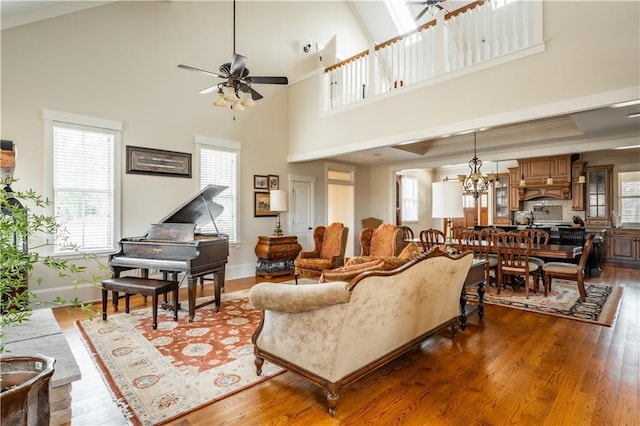 living room with dark wood-type flooring, ceiling fan with notable chandelier, and a towering ceiling