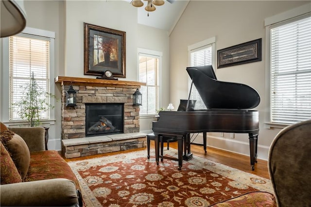 miscellaneous room featuring lofted ceiling, a stone fireplace, wood-type flooring, and plenty of natural light