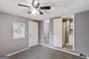 empty room featuring carpet floors, baseboards, a ceiling fan, and visible vents