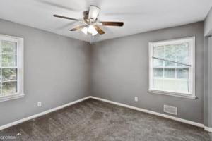 carpeted spare room featuring a healthy amount of sunlight, baseboards, ceiling fan, and visible vents