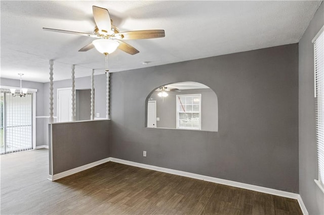 unfurnished room featuring ceiling fan with notable chandelier, baseboards, wood finished floors, and a wealth of natural light
