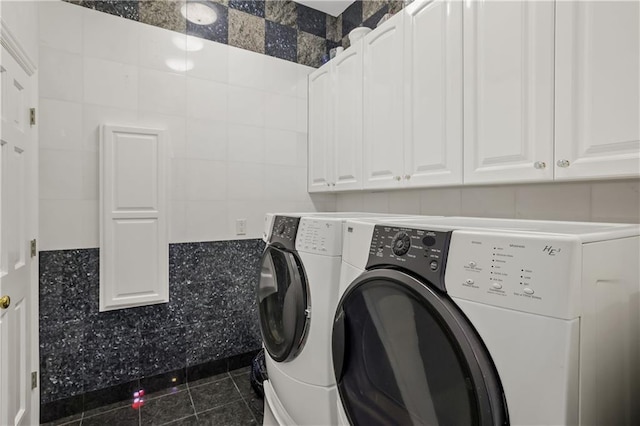 laundry room with cabinets, dark tile patterned floors, washer and clothes dryer, and tile walls