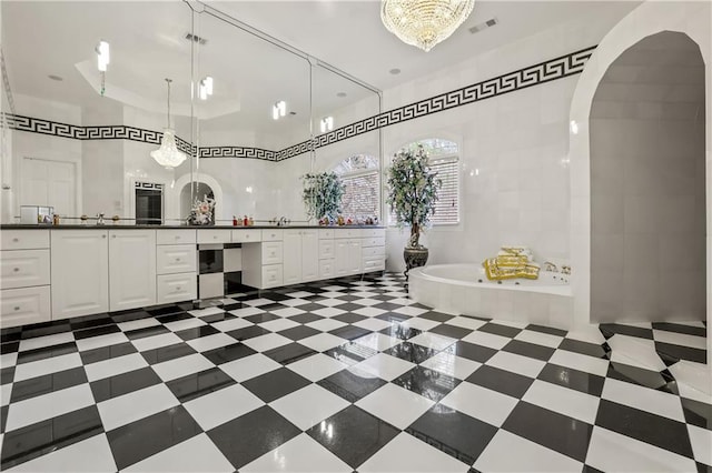 bathroom featuring vanity, tiled tub, and an inviting chandelier