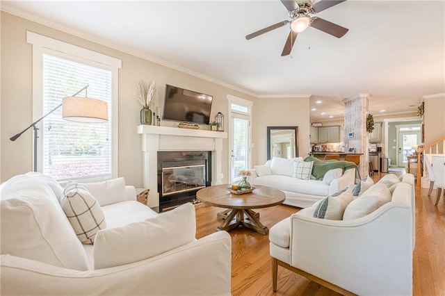 living room featuring ornamental molding, light wood-type flooring, a glass covered fireplace, and a healthy amount of sunlight