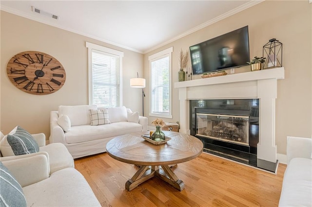 living area featuring wood finished floors, a glass covered fireplace, ornamental molding, and visible vents