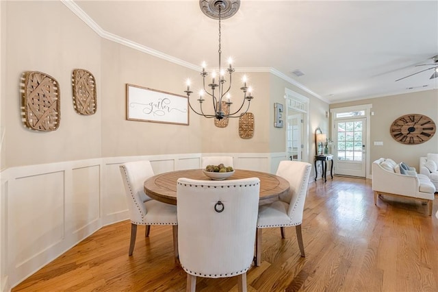 dining space featuring an inviting chandelier, ornamental molding, visible vents, a decorative wall, and wood finished floors