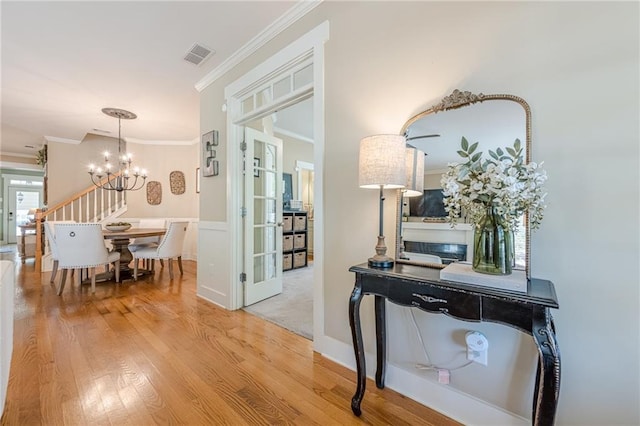 corridor with a notable chandelier, visible vents, crown molding, and wood finished floors