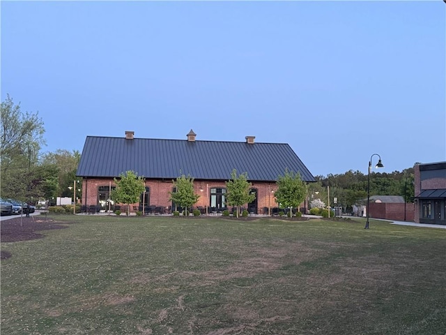 view of front of home with a chimney, metal roof, a front lawn, and brick siding