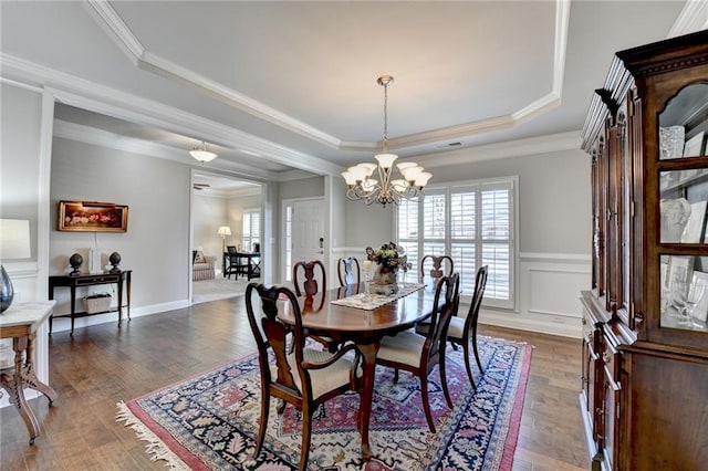 dining space featuring crown molding, a notable chandelier, a raised ceiling, a decorative wall, and dark wood-type flooring