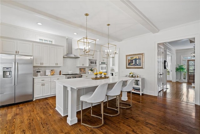 kitchen featuring white cabinetry, wall chimney exhaust hood, hanging light fixtures, a kitchen island with sink, and appliances with stainless steel finishes