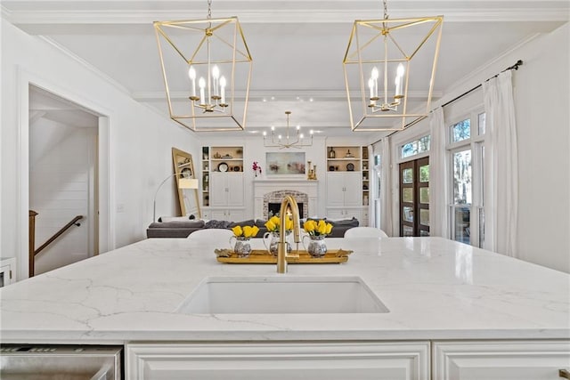 kitchen with light stone counters, a brick fireplace, built in shelves, sink, and pendant lighting